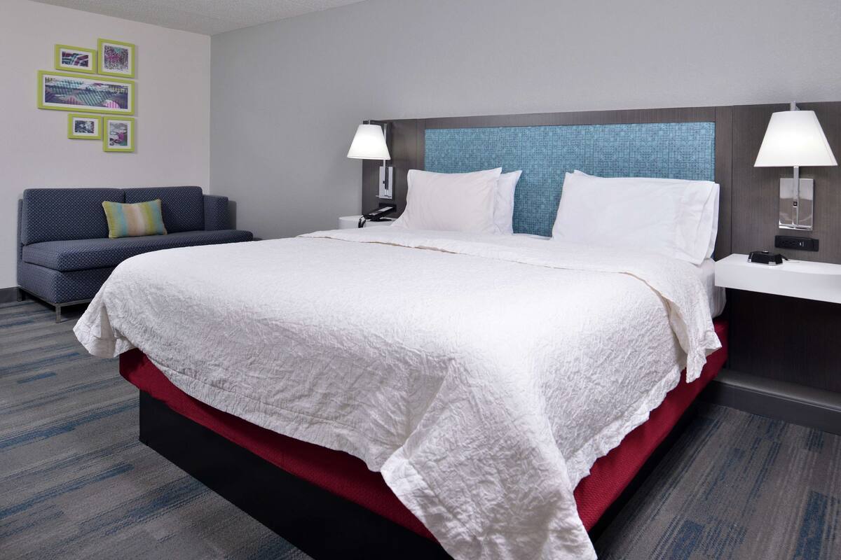 Une chambre d’hôtel avec un grand lit, un canapé bleu et une tête de lit au motif texturé.