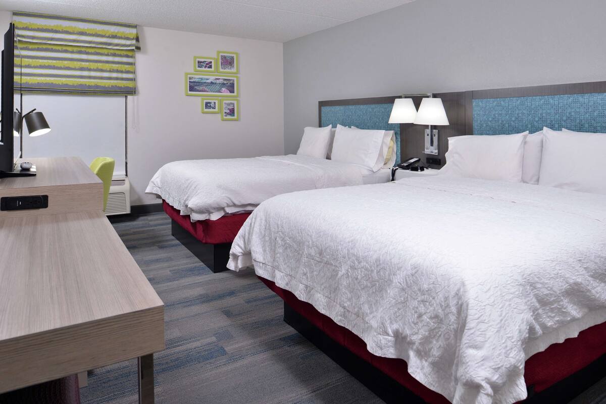 Une chambre d’hôtel avec deux lits, un bureau, une chaise et une lampe.
