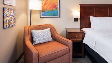 Une chambre d’hôtel avec un lit simple, une table de chevet, une chaise et un mur orné de trois œuvres d’art encadrées.