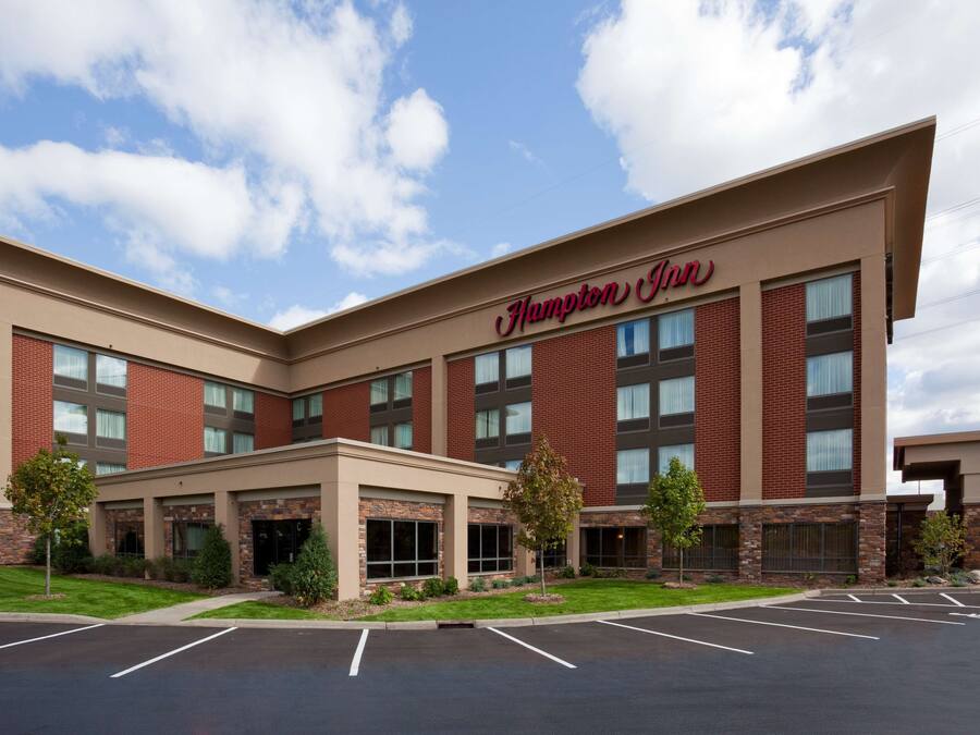 Un hotel Hampton Inn con fachada de ladrillo, ventanas grandes y estacionamiento.