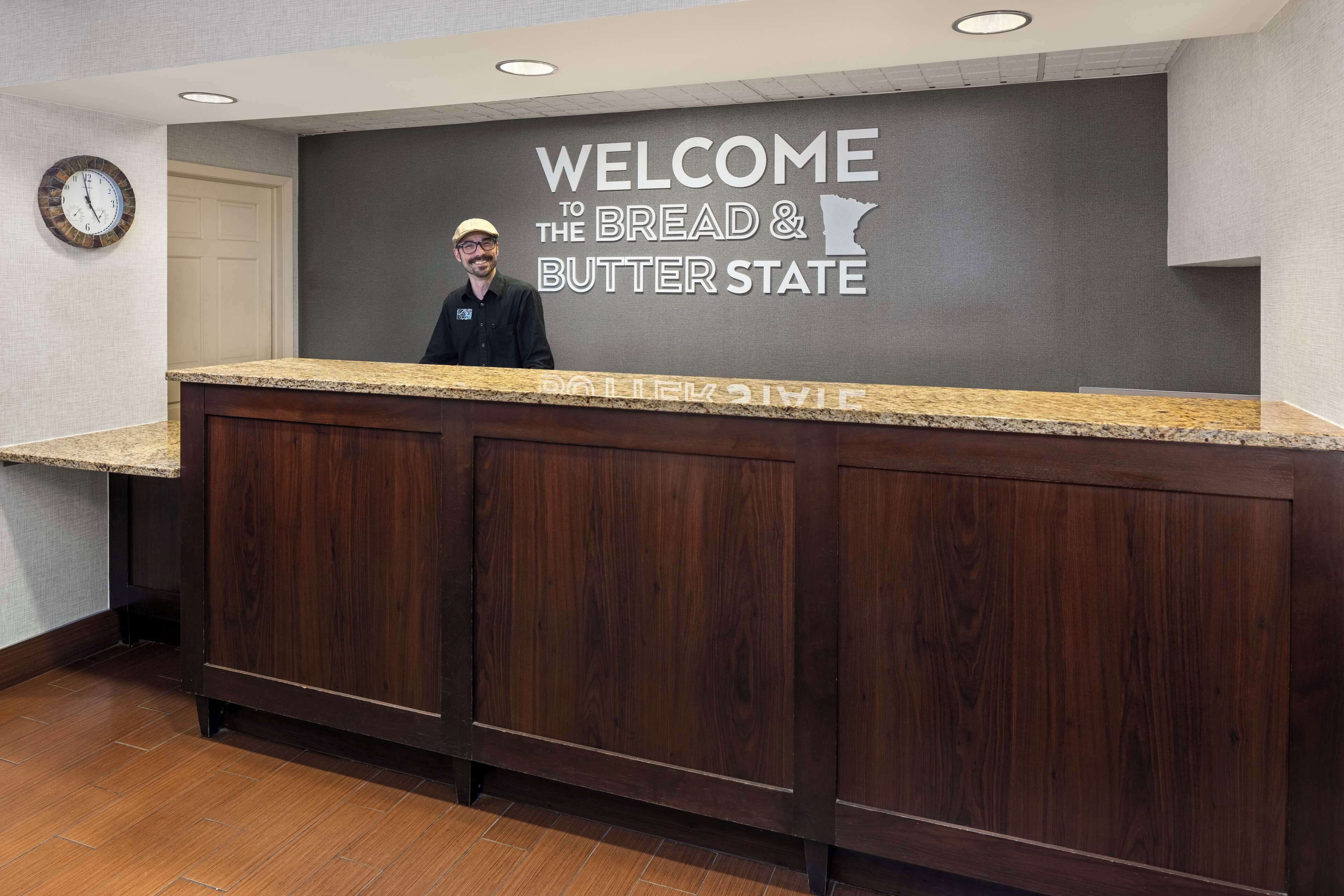 A reception desk with a "Welcome to the Bread & Butter State" sign, wooden paneling, and a clock on the wall.