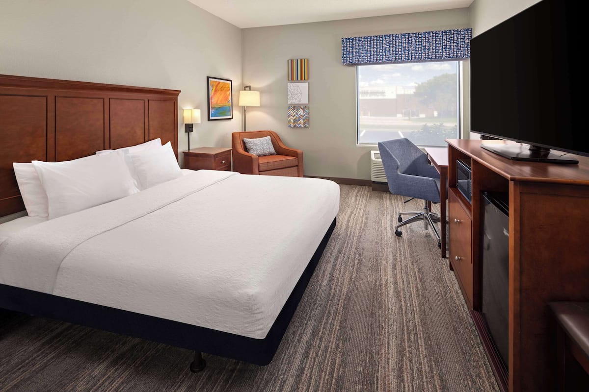 A hotel room with a large bed, a desk with a computer, a TV, and a window with a view of the outside.