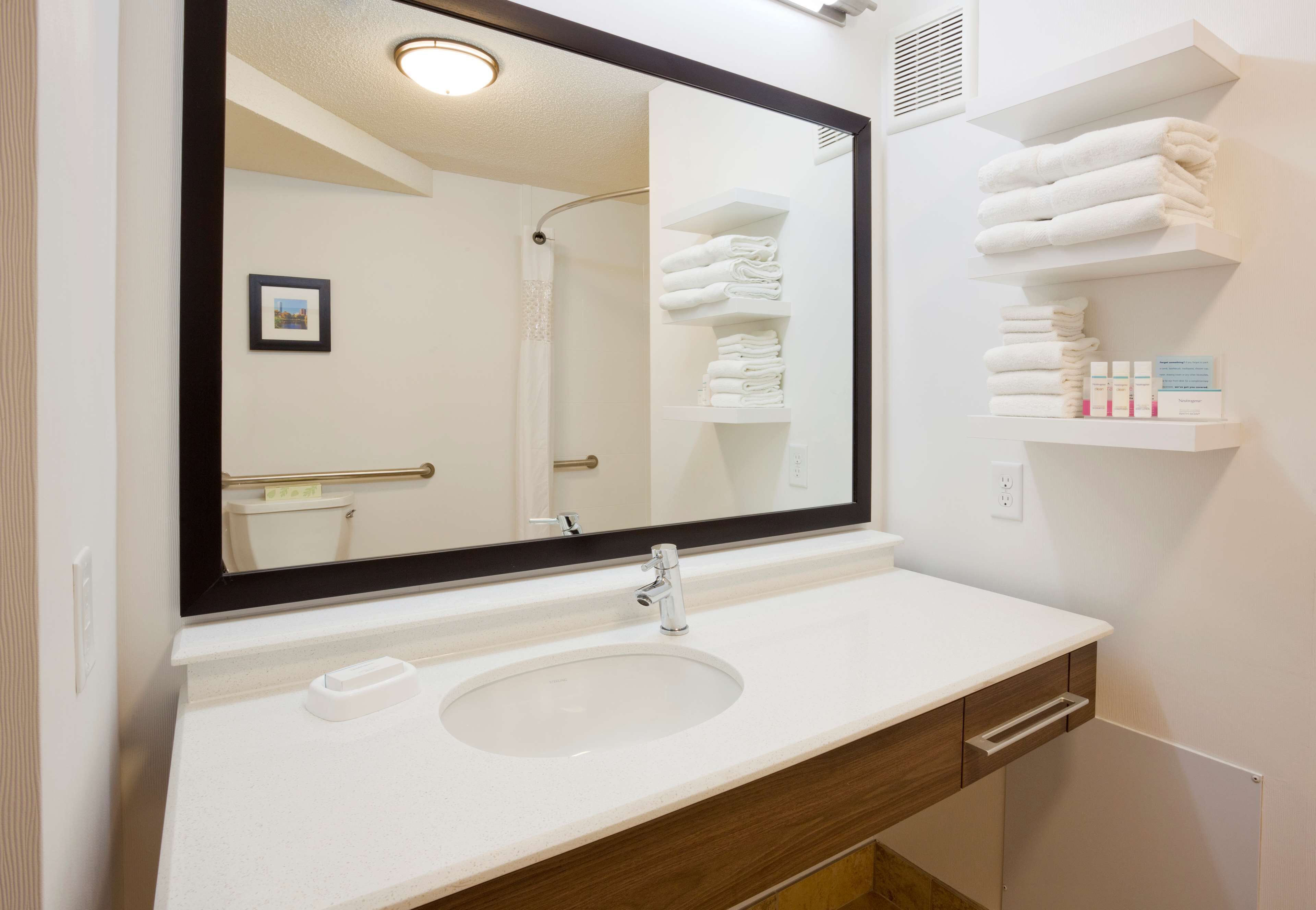 A bathroom with a white sink, a large mirror, and shelves with folded towels.