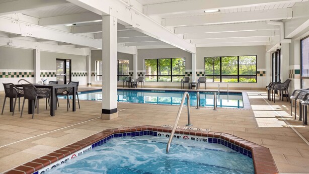 A pool area with a hot tub, lounge chairs, and a dining table.