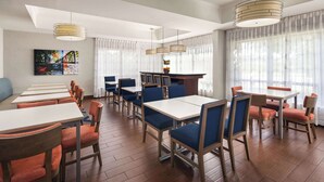 A modern dining area with multiple tables and chairs, a bar area, and large windows with sheer curtains.