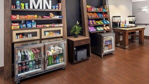 A hotel lobby with a self-service beverage station, snack shelves, and a coffee machine.