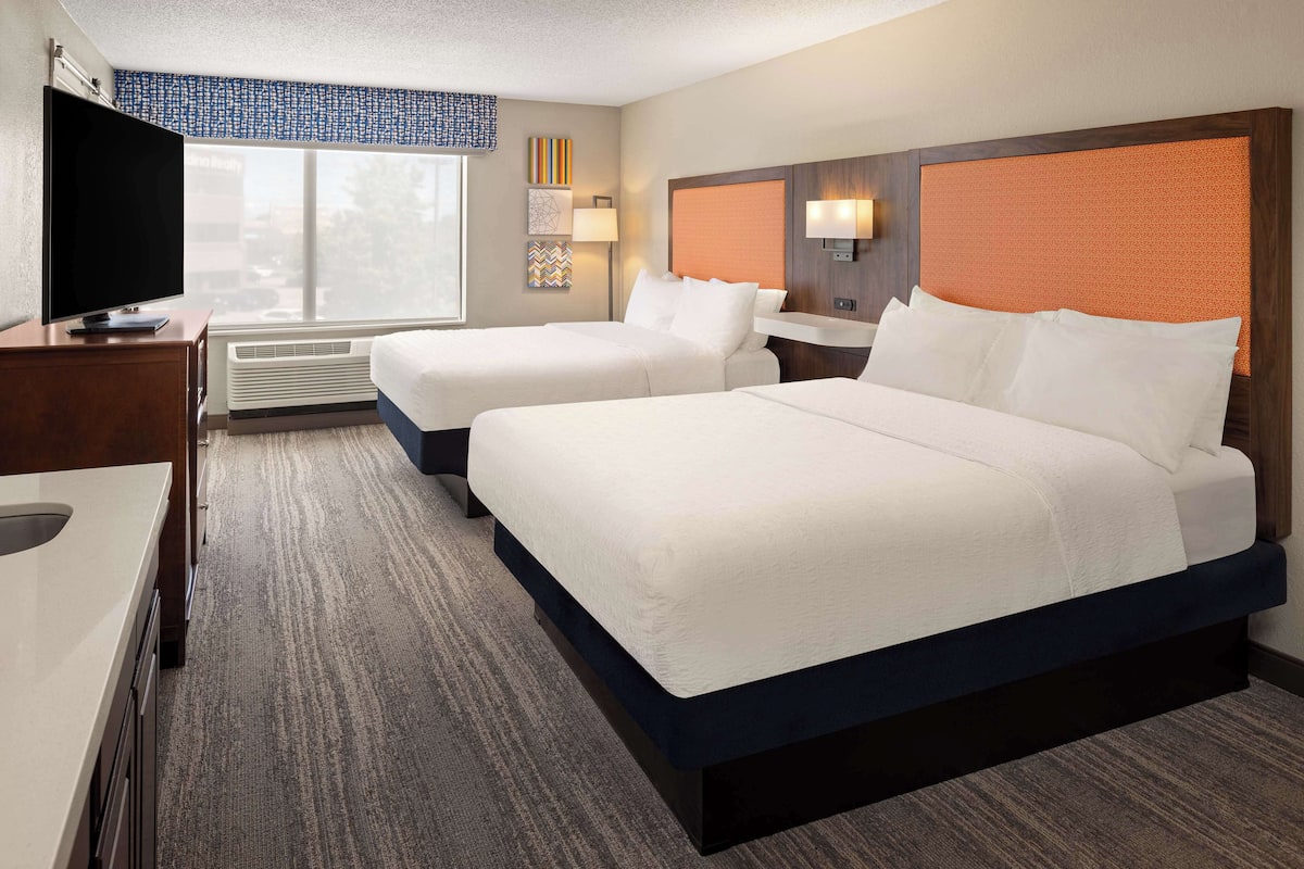 A hotel room with two beds, a TV, a desk, and a window with a view.