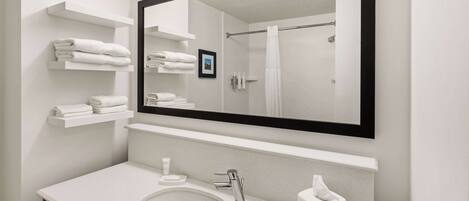 A modern bathroom with a large mirror, white sink, towel racks, and a shower curtain.