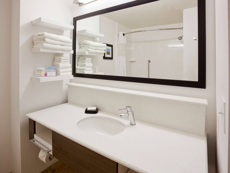 A modern bathroom with a white sink, a large mirror, and neatly folded towels on a shelf.