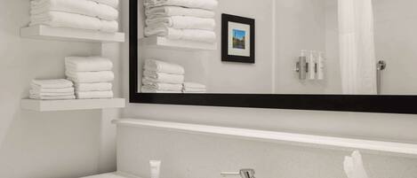 Un baño moderno con un lavamanos blanco, un espejo grande y toallas ordenadas en estantes.