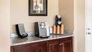 A kitchenette with a coffee machine, a framed artwork, and a clock on the wall. - Rodeway Inn Oxford (Oxford)