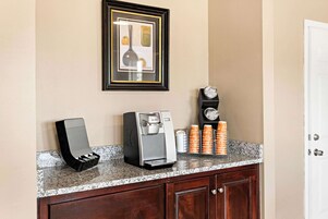 Una kitchenette con una cafetera, una obra de arte enmarcada y un reloj en la pared.