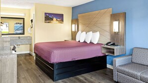 A hotel room with a bed, a nightstand, a chair, a desk with a phone, and a picture on the wall. - Rodeway Inn Oxford (Oxford)