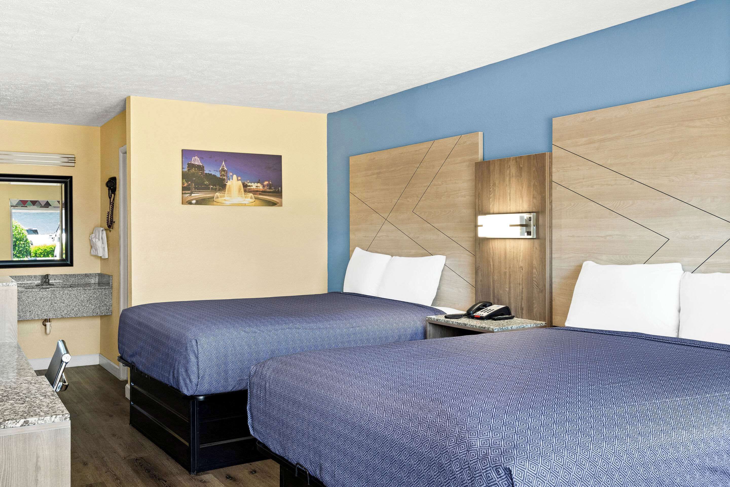 Una habitación de hotel con dos camas, una mesita de noche, un escritorio, un teléfono y un cuadro en la pared.
