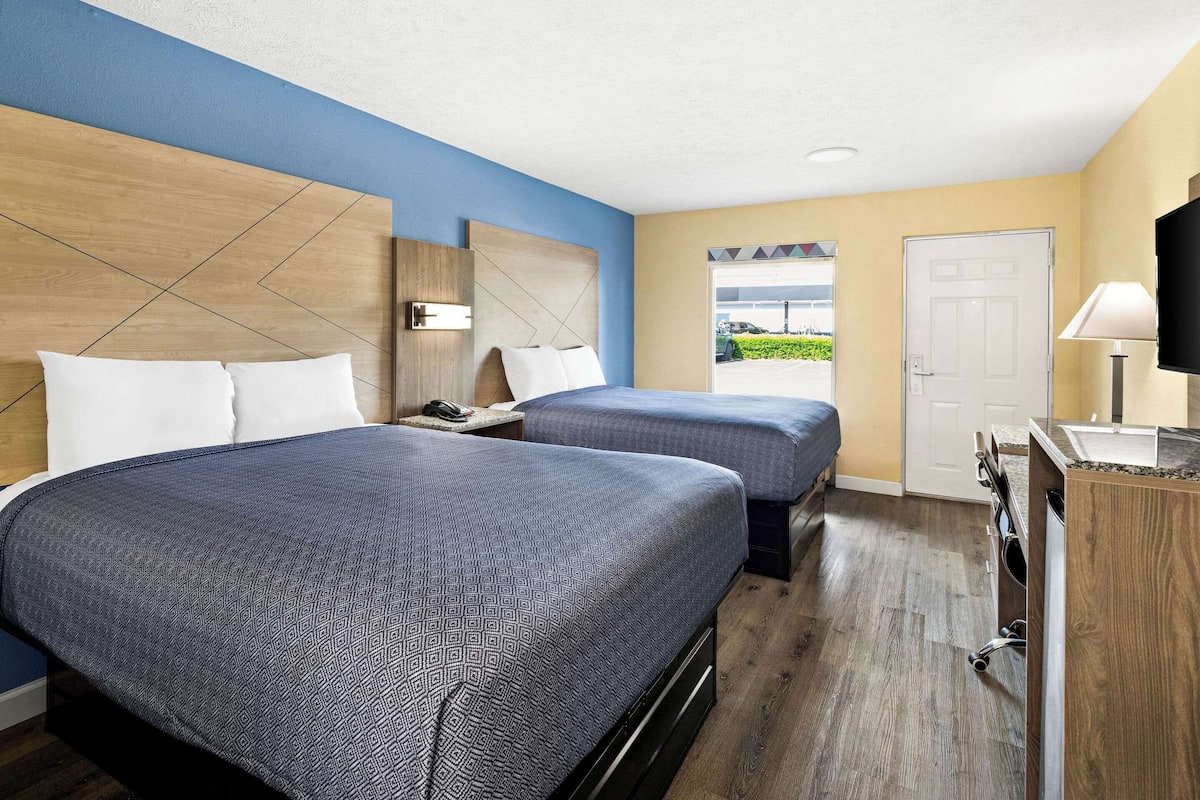 A hotel room with two beds, a wooden headboard, a desk with a lamp, and a TV.