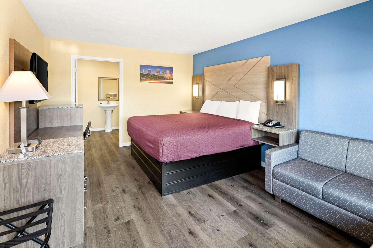 A hotel room with a bed, a desk, a chair, a sofa, a TV, and a bathroom.