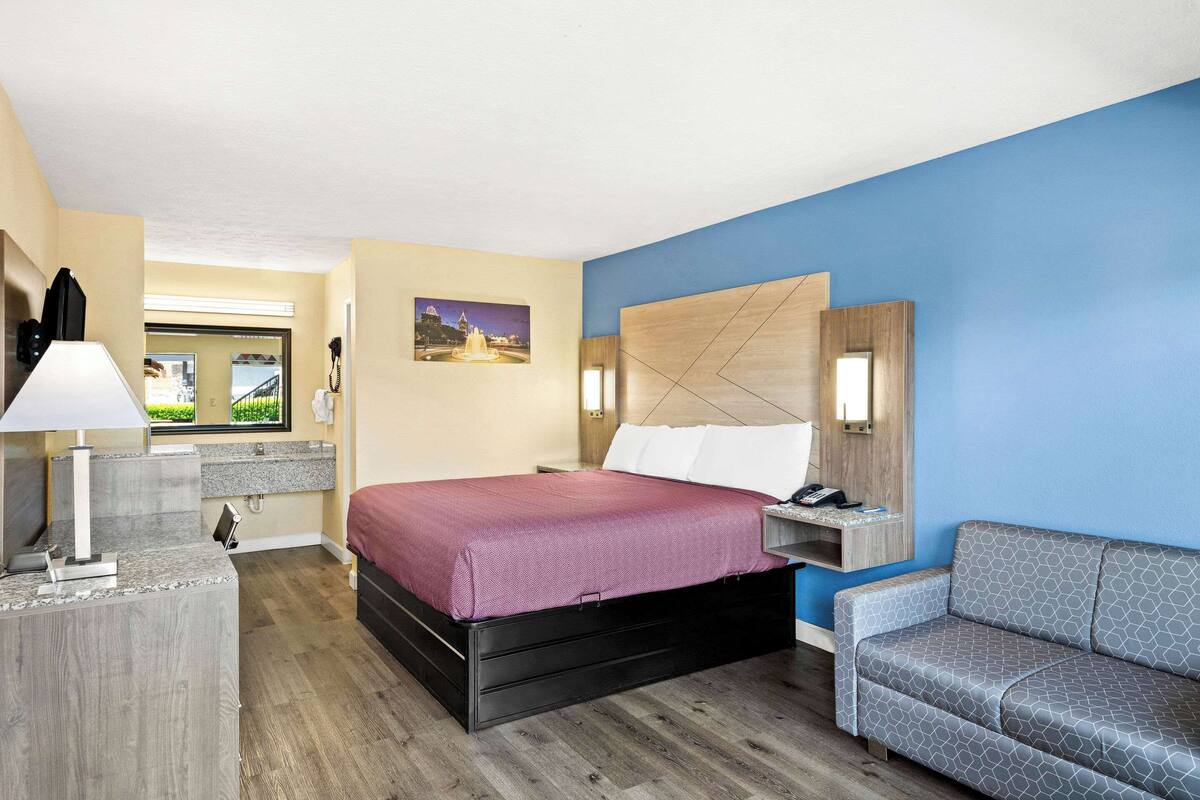A hotel room with a bed, a desk, a chair, a nightstand, and a wall-mounted TV.