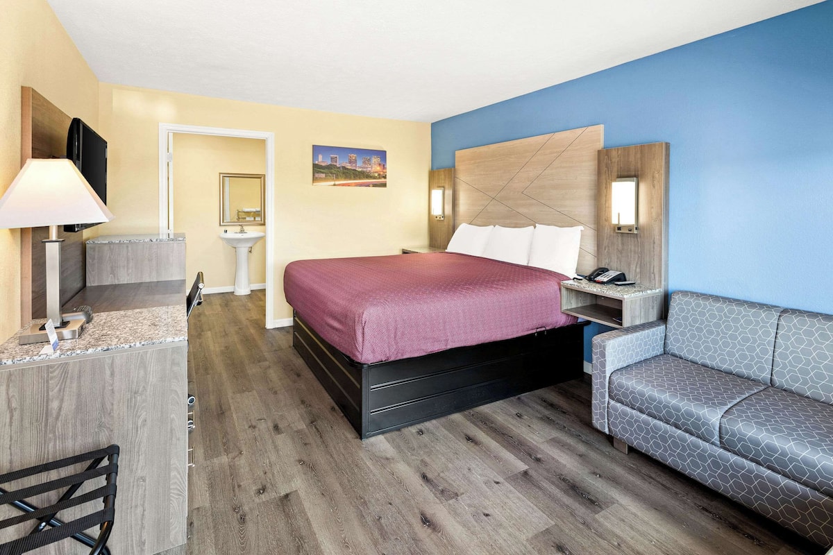 A hotel room with a bed, a desk, a chair, a sofa, a TV, and a bathroom.
