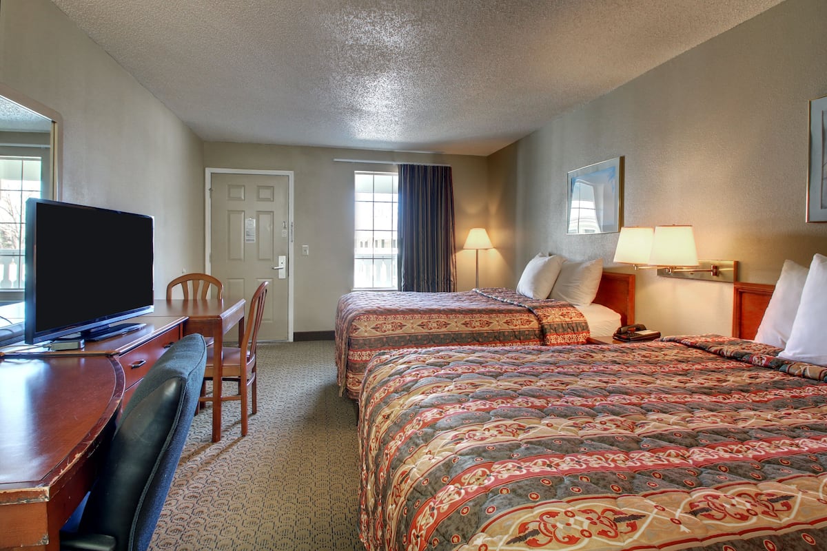 A hotel room with two beds, a desk with a TV, a chair, and a door.