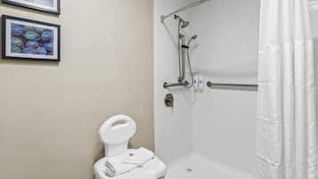 A bathroom with a shower, toilet, and framed artwork on the wall.