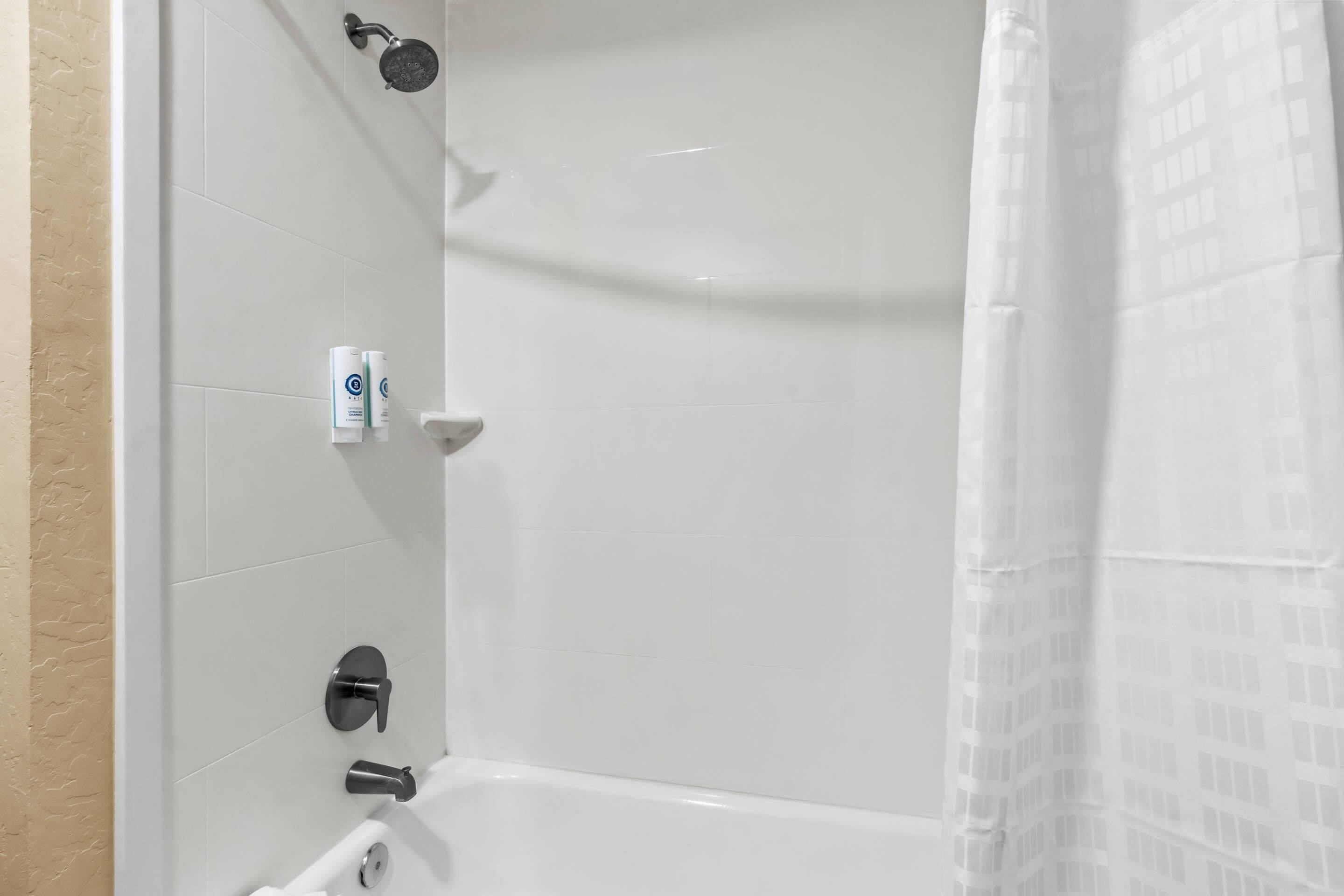 Ein Badezimmer mit weißen Fliesen, einer Duschbrause, einer Toilette und einem Handtuchhalter.