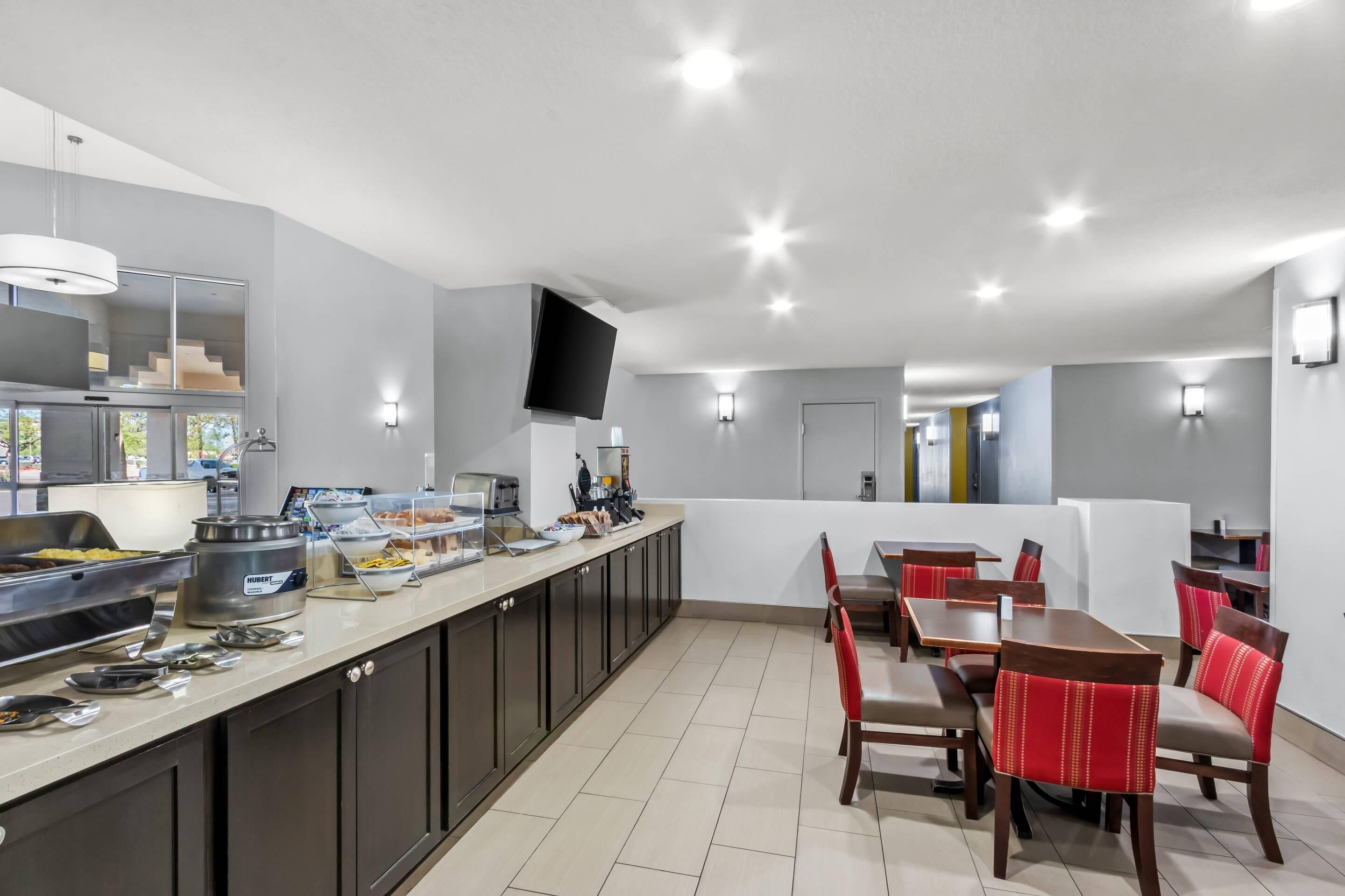 A modern hotel dining area with a buffet, seating, and a TV mounted on the wall.