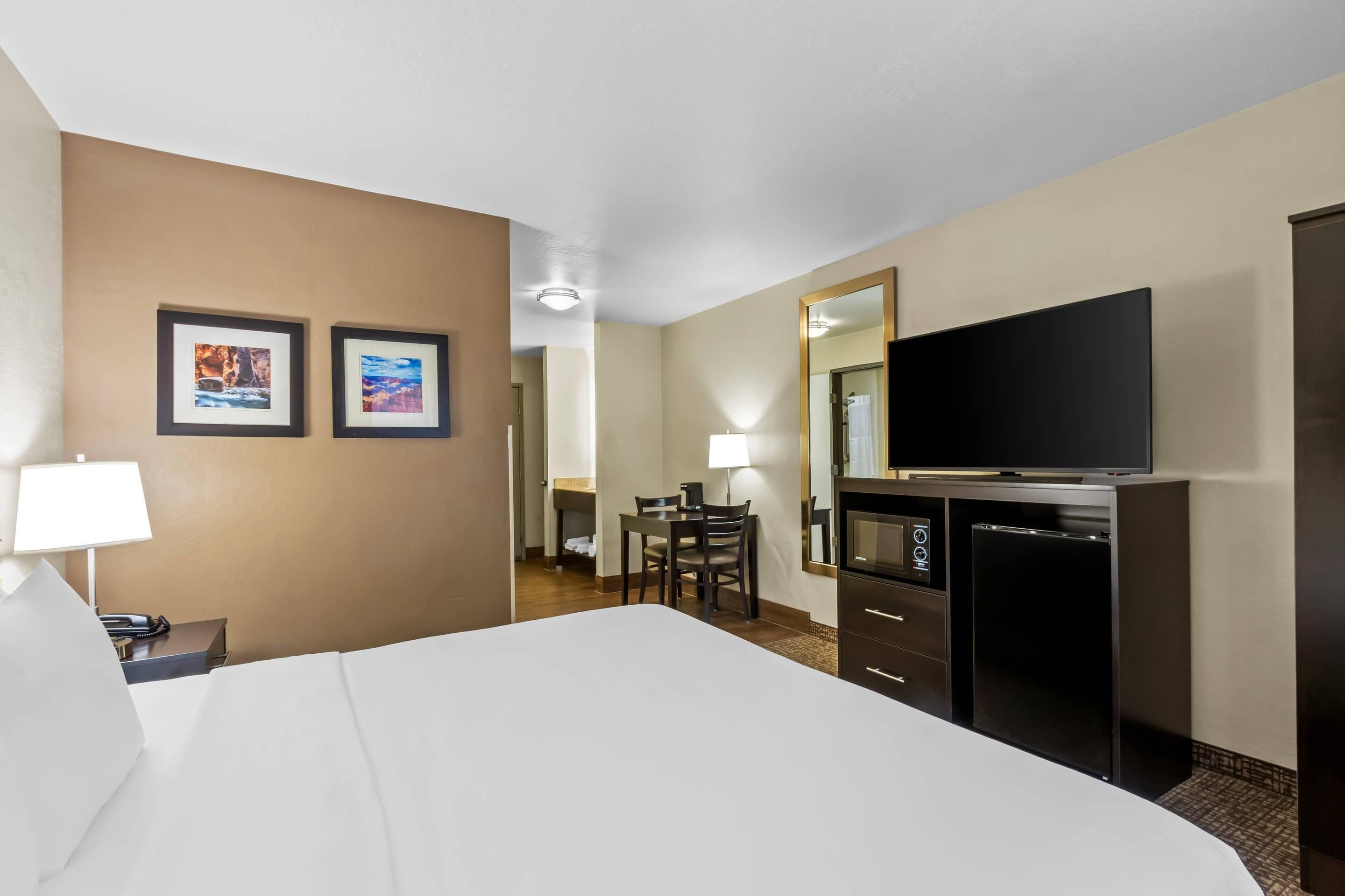 A hotel room with a large bed, a desk with a chair, a television, a mirror, and two framed pictures on the wall.