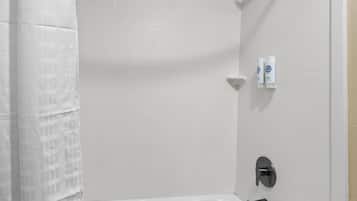 A white tiled bathroom with a shower curtain, a bathtub, and two hand dryers mounted on the wall.