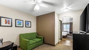 A hotel room with a green sofa, a dining table, and chairs, a ceiling fan, and framed pictures on the wall.