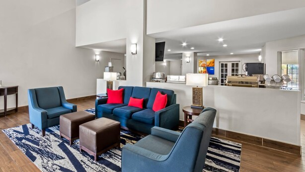 A modern hotel lobby with a blue sofa set, a coffee table, and a bar area with a television.