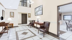 Een ruime lobby met een hoge plafond, een kroonluchter, een zithoek met stoelen en een tafel, en een inlijsting kunstwerk aan de muur.