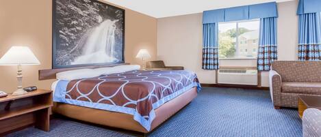 A hotel room with a bed, two bedside lamps, a large framed picture of a waterfall, a window with blue curtains, and a sofa.