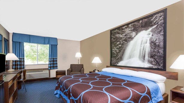 Een hotelkamer met een groot bed, een bureau met een computer, een stoel, twee lampen en een groot raam met gordijnen.