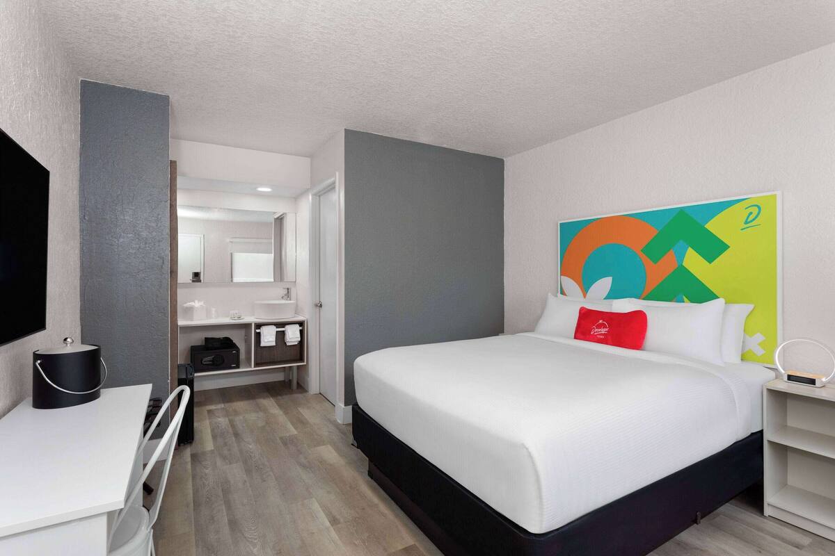 A modern hotel room with a large bed, a desk, and a bathroom visible through an open door.