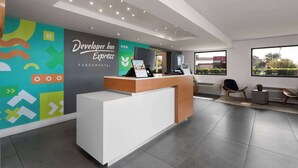 A modern hotel reception area with a reception desk, a colorful wall design, and a seating area with a view of the outdoors. - Travelodge by Wyndham Orlando Lake Buena Vista South (Kissimmee)