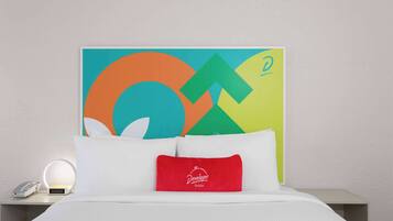 A hotel room with a bed, a nightstand with a lamp, and a colorful abstract painting on the wall.