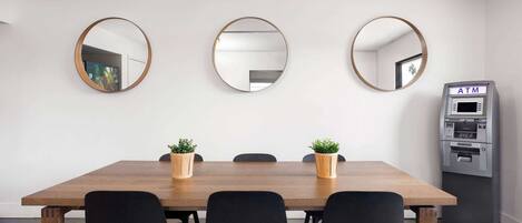 Un salón de conferencias con una mesa de madera, sillas negras, tres espejos redondos y un cajero automático pequeño.