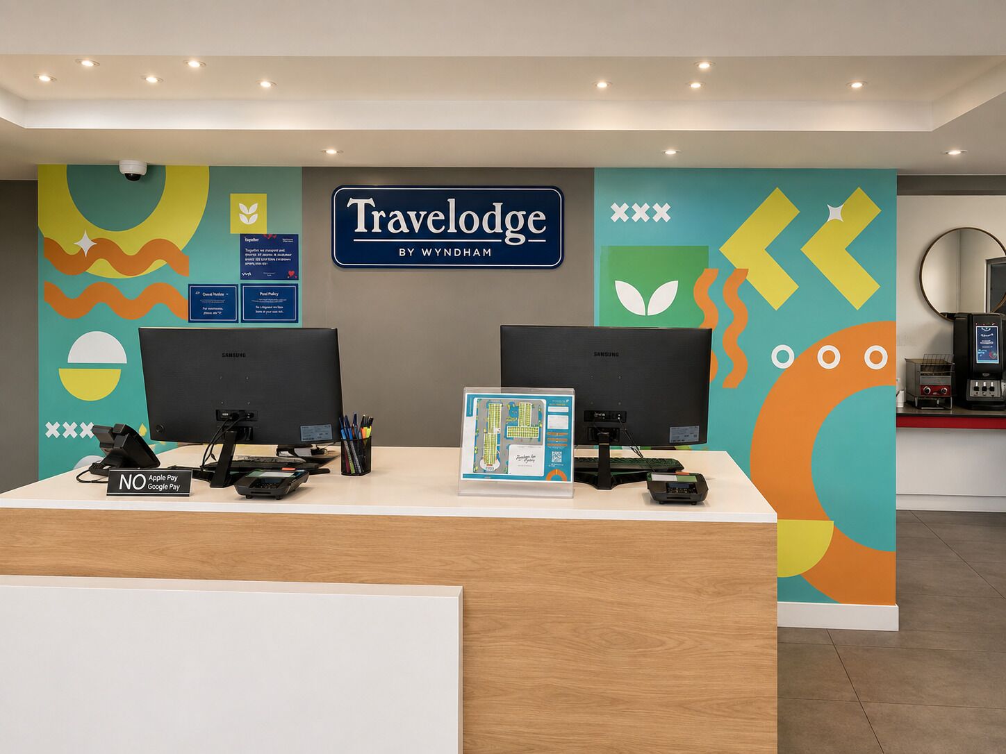A reception desk with two monitors, a sign for Travelodge by Wyndham, and a no Apple Pay/Google Pay sign.