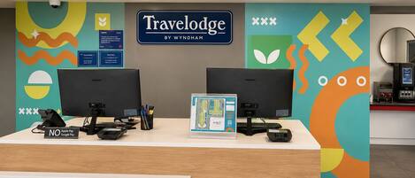 Una recepción con dos monitores, un cartel de Travelodge by Wyndham y un letrero que indica que no se aceptan Apple Pay/Google Pay.