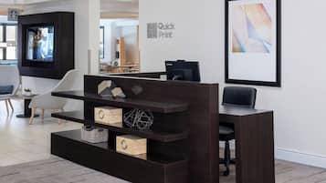 Una mesa de recepción con una pantalla digital, una obra de arte abstracta enmarcada y un monitor Lenovo.