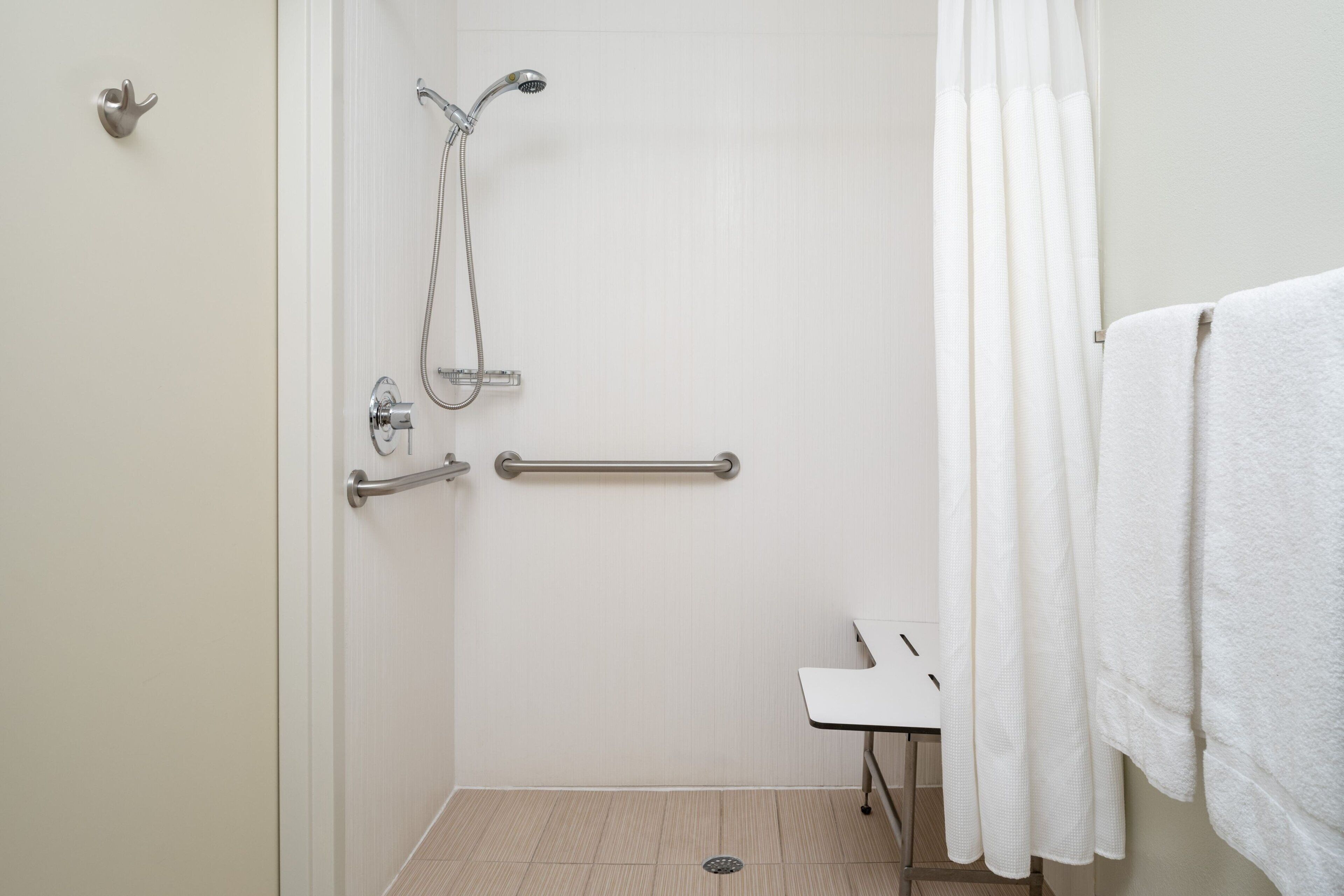 A walk-in shower with a grab bar, a white towel, and a showerhead.