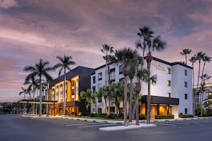 Un hotel Courtyard by Marriott con un diseño moderno, que cuenta con un estacionamiento y palmeras.
