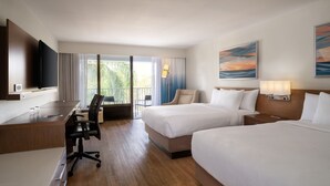 Una habitación de hotel con escritorio, dos camas, televisión y balcón con cortinas.