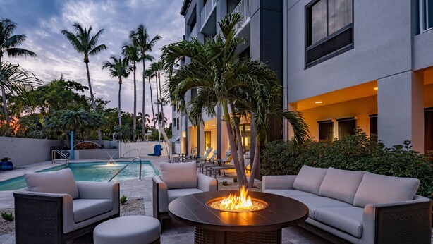 Zona junto a la piscina con un hogar, mobiliario exterior y palmeras.