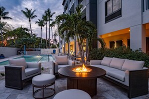 Un espace aménagé au bord de la piscine, avec un foyer, du mobilier d’extérieur et des palmiers.