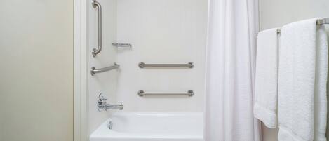 Une salle de bain équipée d’une baignoire, de barres d’appui et d’un rideau de douche.