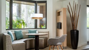 Una sala moderna con un sofá seccional, una mesa redonda, un sillón gris, un jarrón alto con ramas y un televisor de pantalla plana montado en la pared.