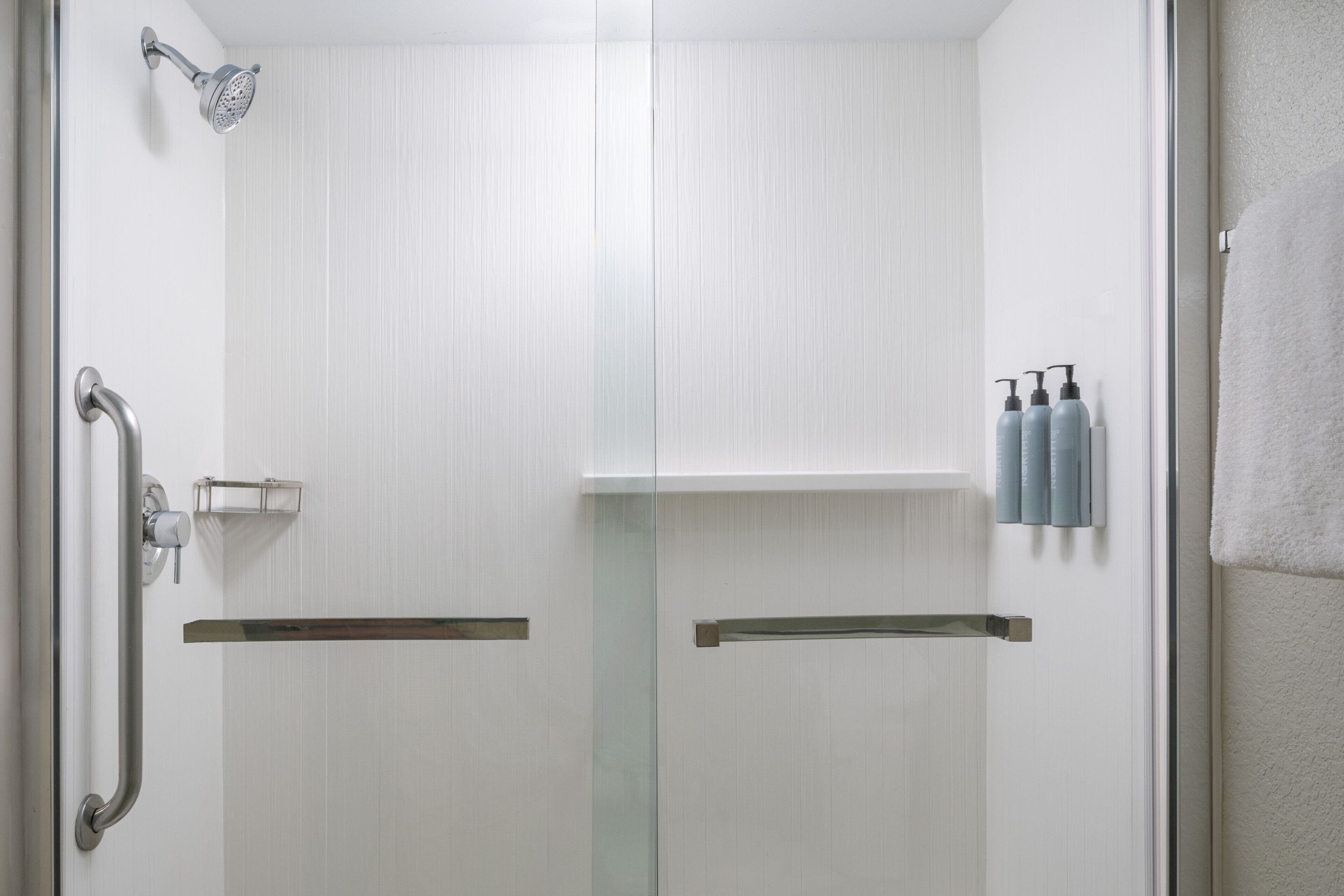 A modern bathroom with a glass shower enclosure, a handrail, and a towel rack with bottles.
