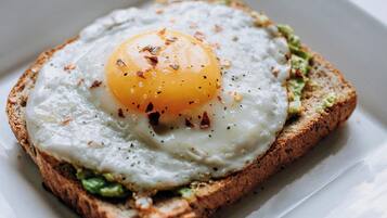 A square plate with a toasted bread topped with a fried egg and green spread.