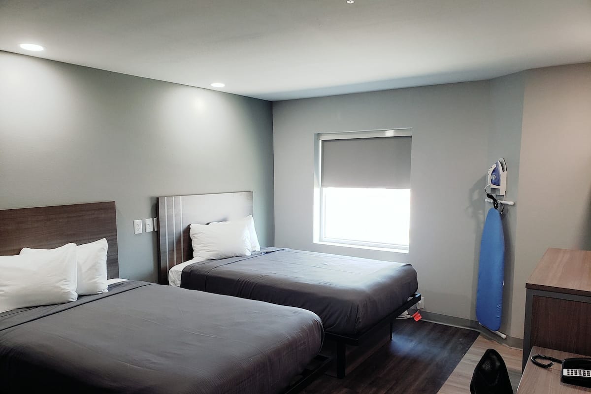 A hotel room with two beds, a window with a view, a desk with a telephone, and a wall-mounted ironing board.